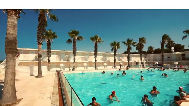 Una piscina con palmeras y un edificio al fondo.