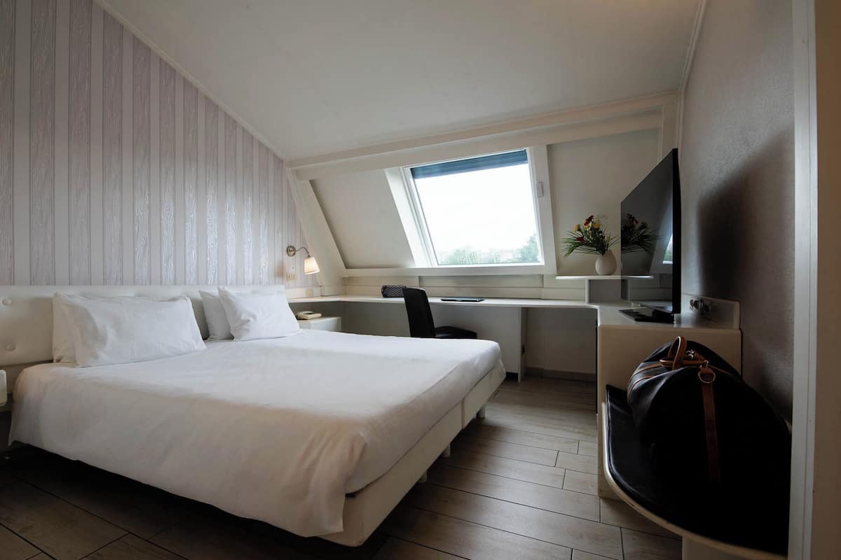 A modern hotel room with a bed, desk, and TV.
