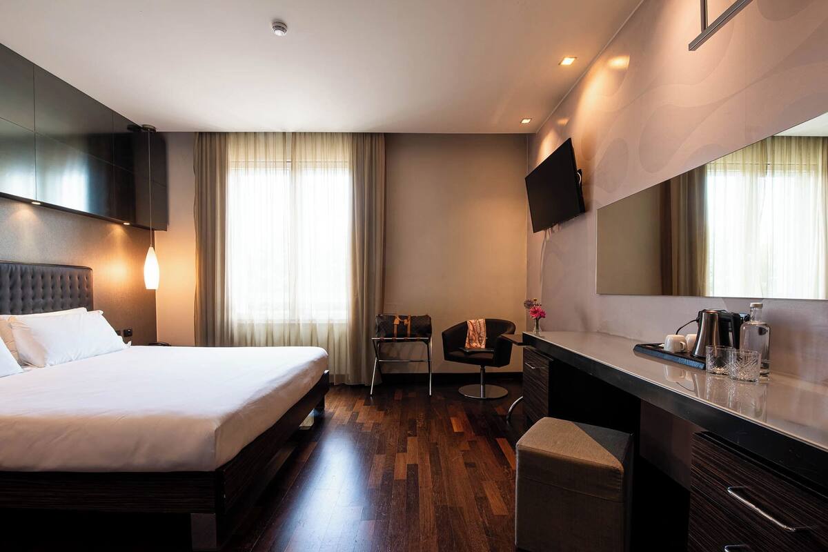 A hotel room with a bed, a desk, a chair, a TV, and a mirror.
