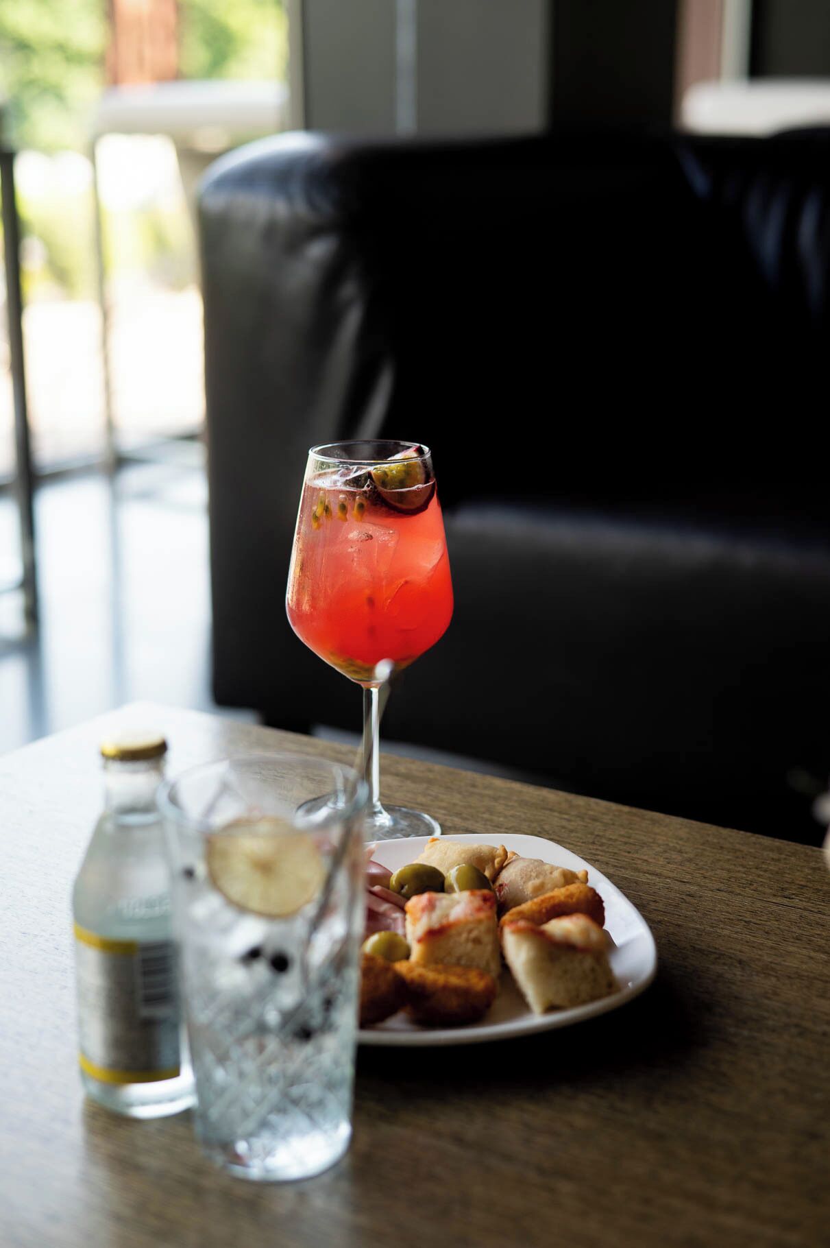 Una mesa con una copa de cóctel rojo, una botella de agua y un plato de comida.