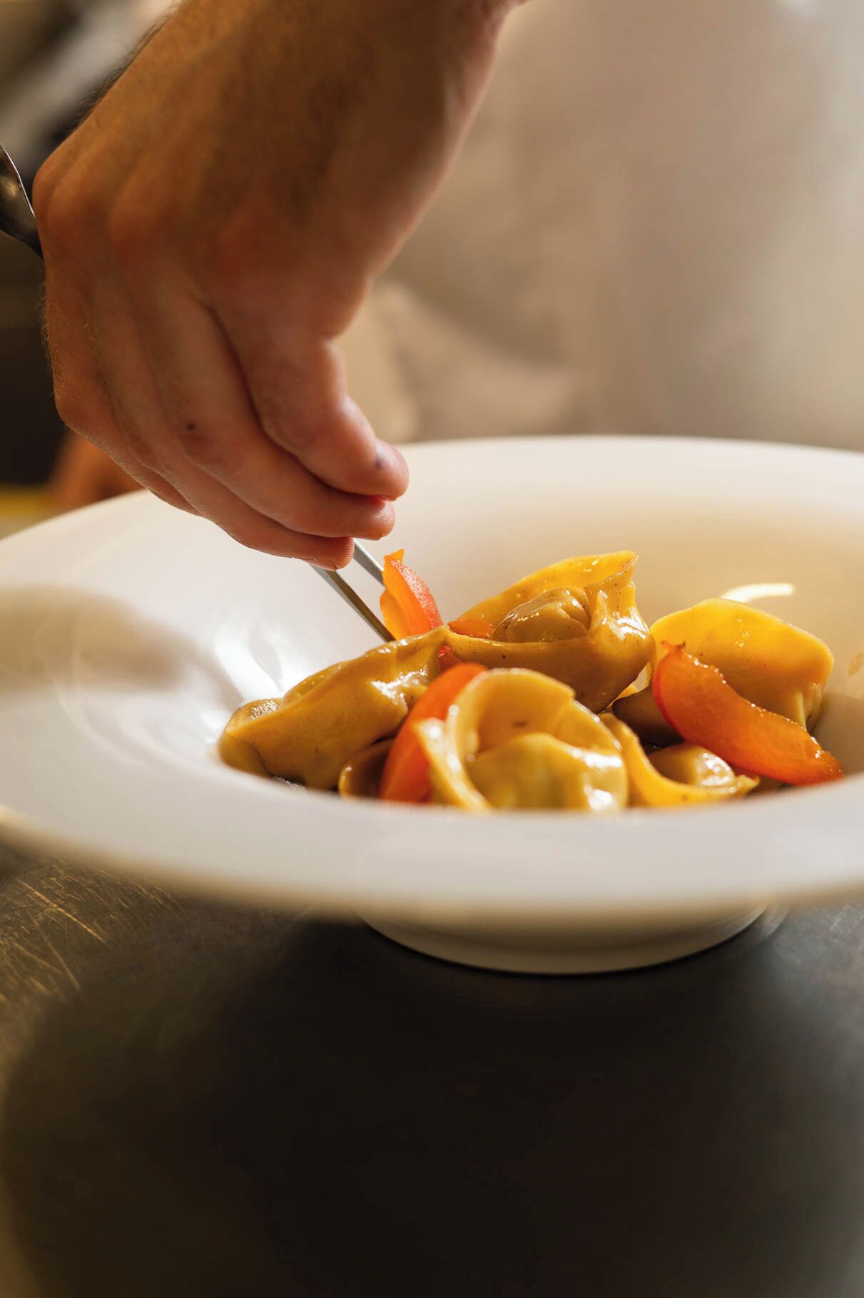 Una persona mangia ravioli con salsa e verdure da un piatto bianco usando una forchetta.