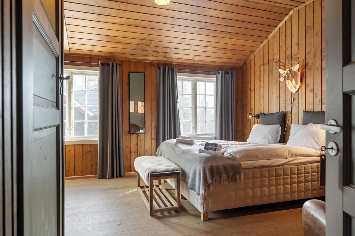 Ein Schlafzimmer mit Holzbalkendecke, einem Bett mit weißer Bettwäsche, einer Bank und einem Spiegel an der Wand.