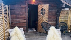 A rustic cabin with a wooden exterior, a door with a diamond-shaped window, and a porch with two lounge chairs covered in white fur. - Herangtunet Mountain Lodge Norway (Øystre Slidre)