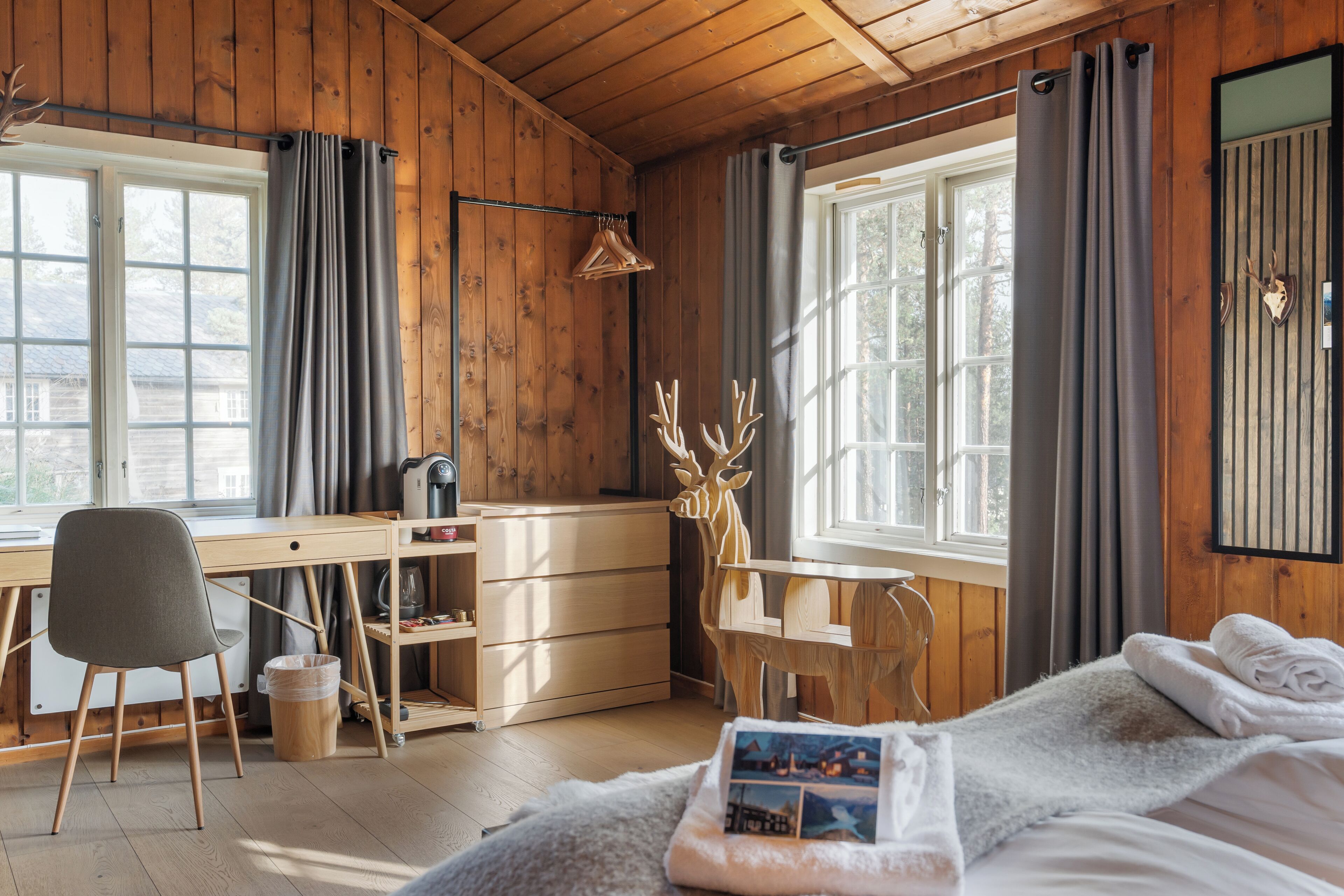 A wooden cabin room with a bed, a desk, and a chair.