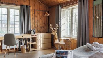 A wooden cabin room with a bed, a desk, and a chair.