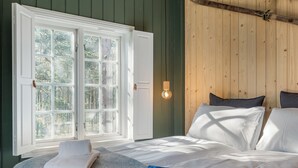 A bedroom with a large window, a bed with white linens, and a wall-mounted light fixture. - Herangtunet Mountain Lodge Norway (Øystre Slidre)