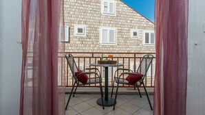 A balcony with two chairs and a table, overlooking a building with stone walls and windows. - Apartments Lapad (Dubrovnik)