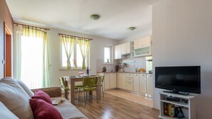 A modern living room with a sofa, a flat-screen TV, and a dining area with a table and chairs. - Apartments Lapad (Dubrovnik)