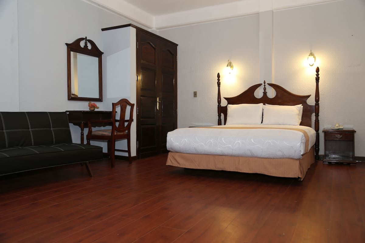 A bedroom with a wooden bed, a wooden nightstand, a wooden chair, a wooden desk, and a mirror on the wall.