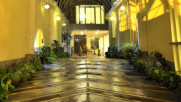 Uma galeria coberta com teto de vidro, que leva à entrada de um edifício.