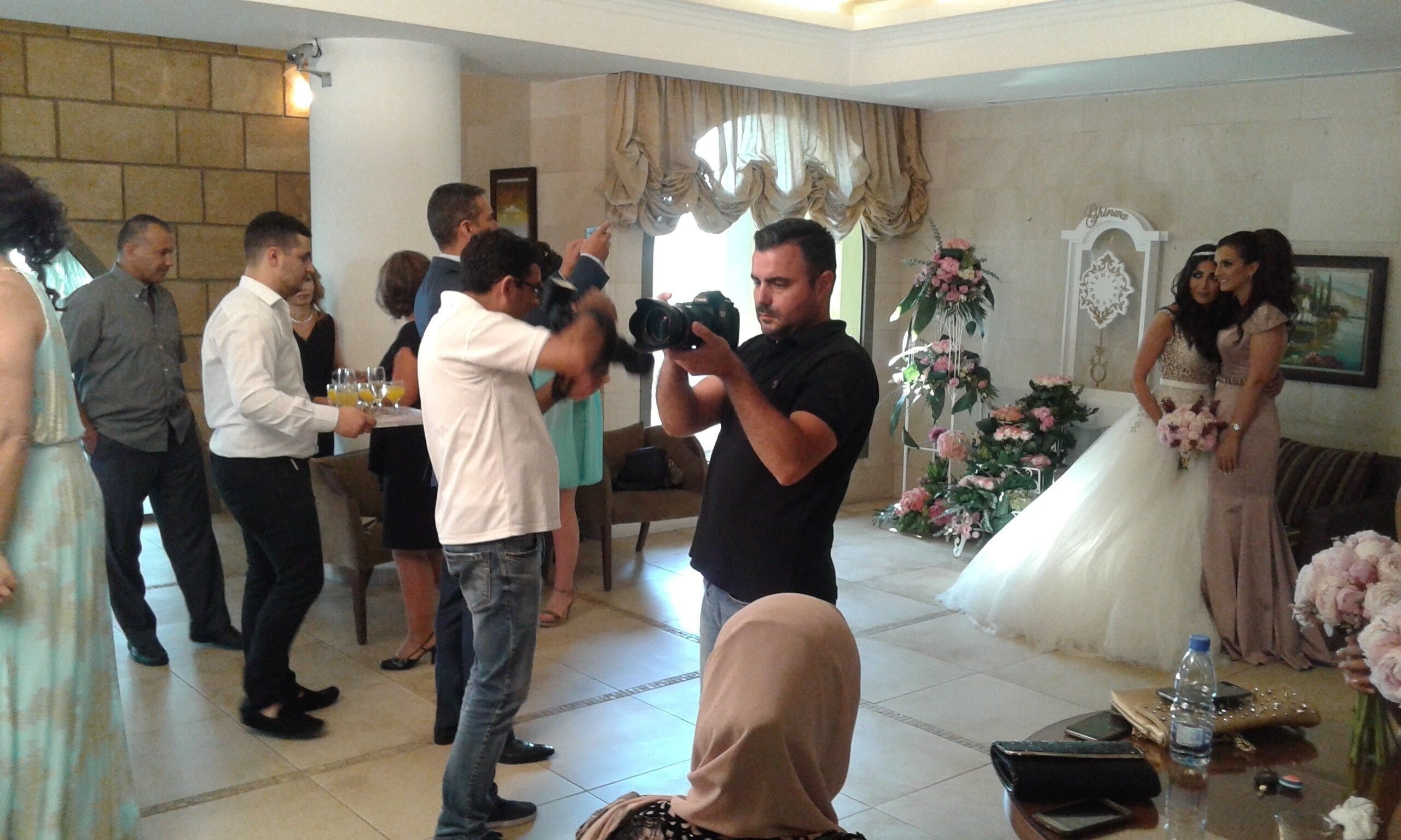 Una recepción de boda con un fotógrafo tomando fotos, invitados reunidos y una novia con un vestido blanco.