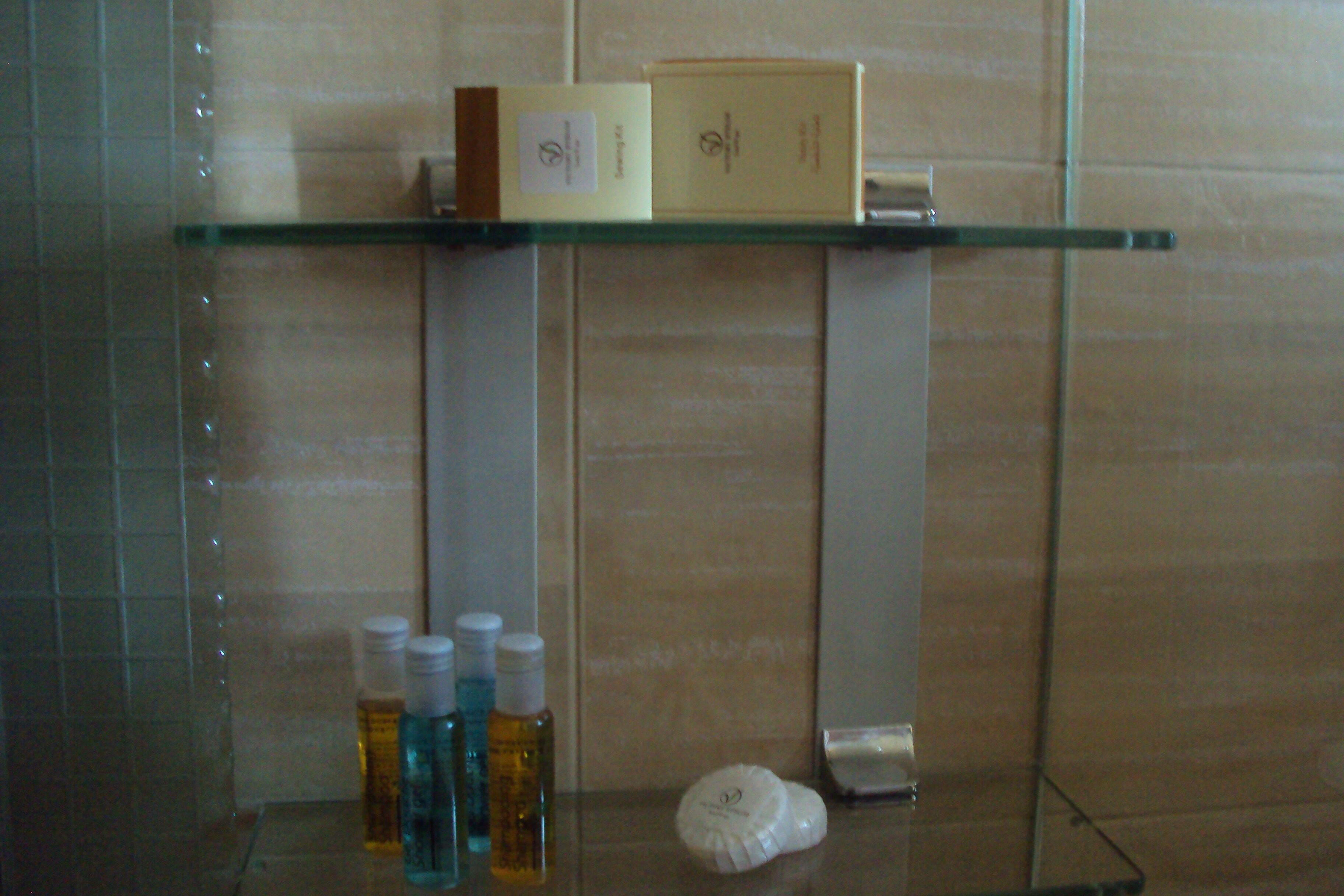 A bathroom with a glass shelf holding toiletries and a box.