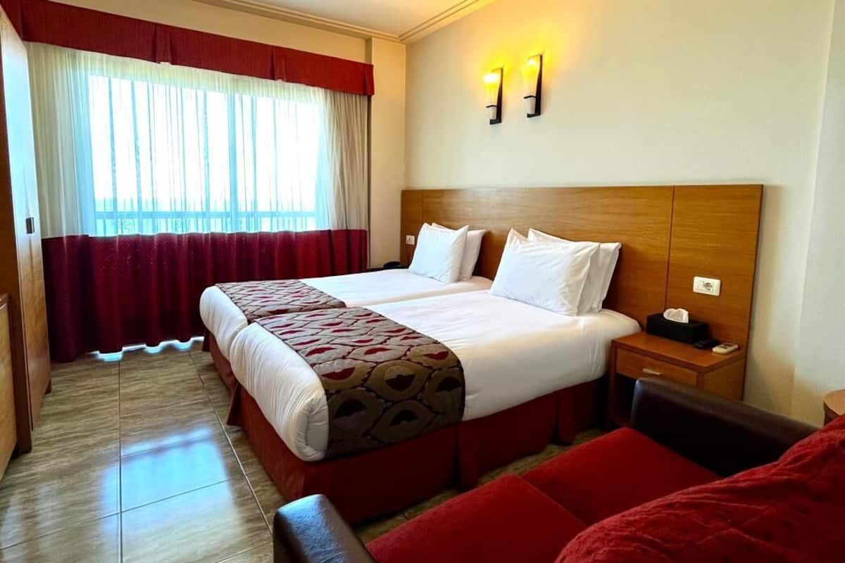 Une chambre d’hôtel avec un grand lit, une tête de lit en bois, deux tables de chevet et une chaise rouge.