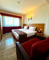 Una habitación de hotel con una cama grande, un cabecero de madera, dos mesitas de noche y una silla roja.