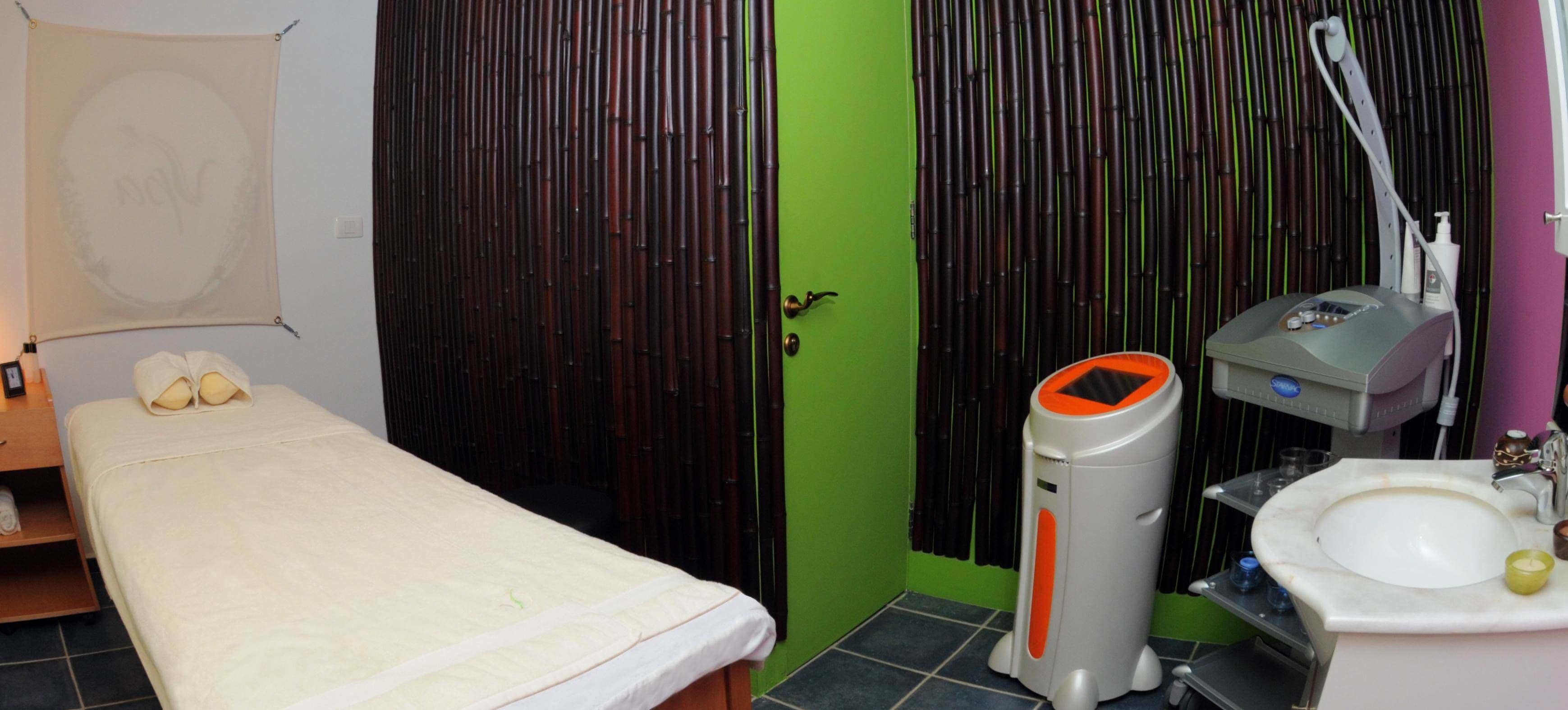 Una habitación con cama, sillón de masaje, un lavamanos pequeño y un muro de cortinas de bambú.