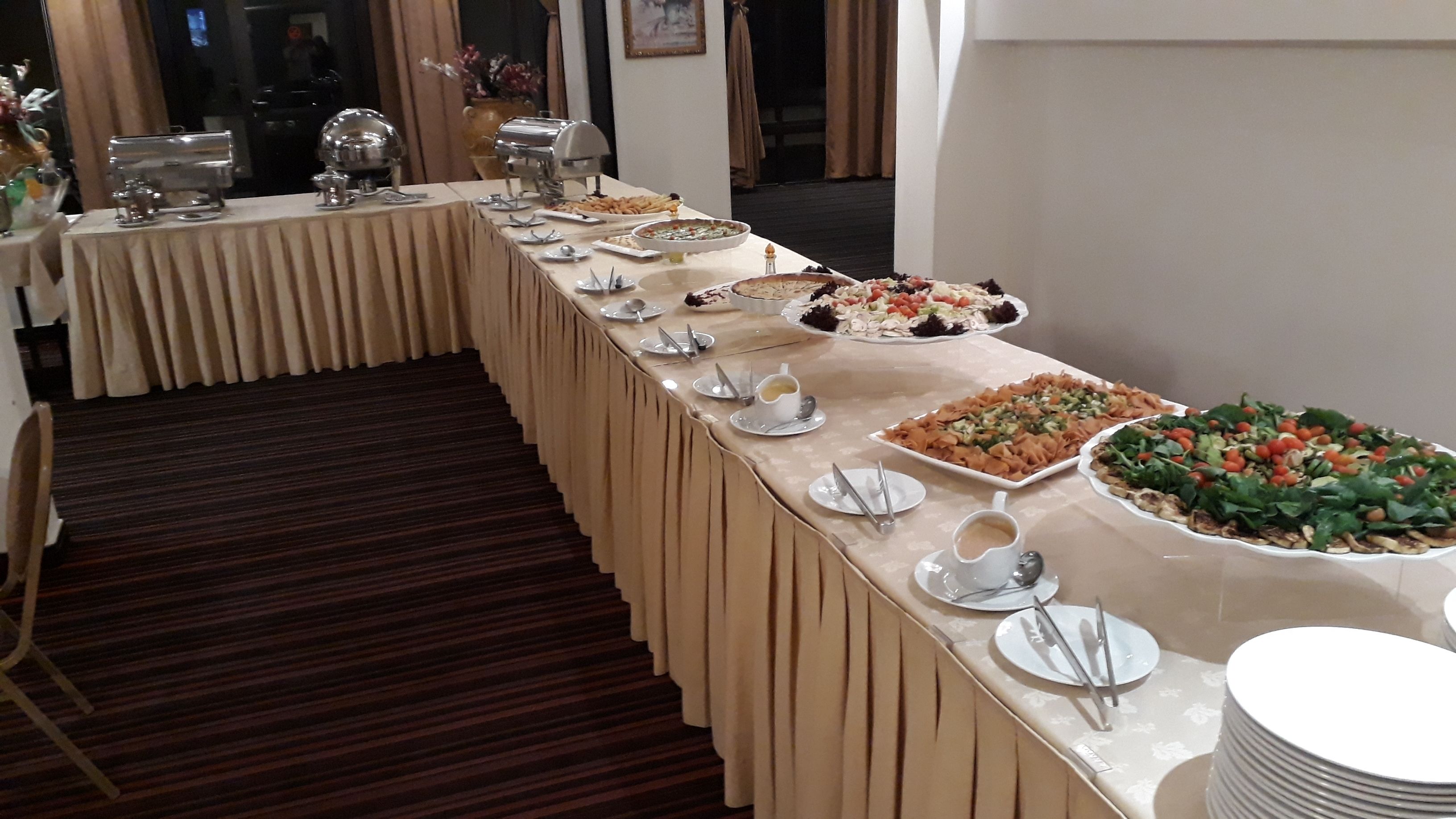 Una mesa de buffet con diversos platos y utensilios, un suelo alfombrado y un espejo que refleja parte de la habitación.