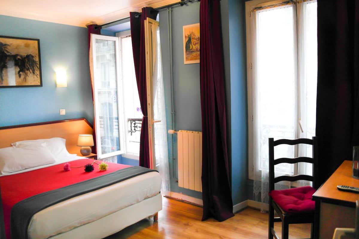 Une chambre à coucher avec un lit, une chaise, une table et une fenêtre avec des rideaux.