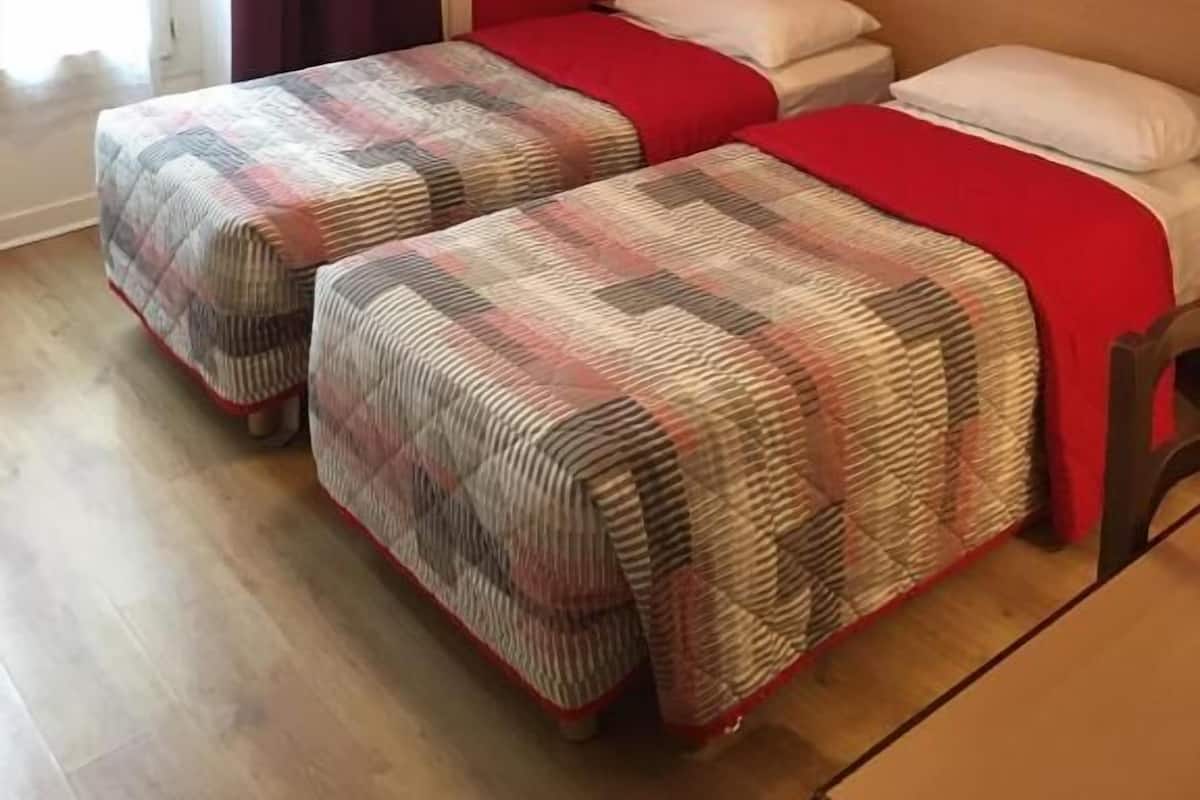 Une chambre avec deux lits, des murs rouges, un plancher en bois et une porte avec un rideau.
