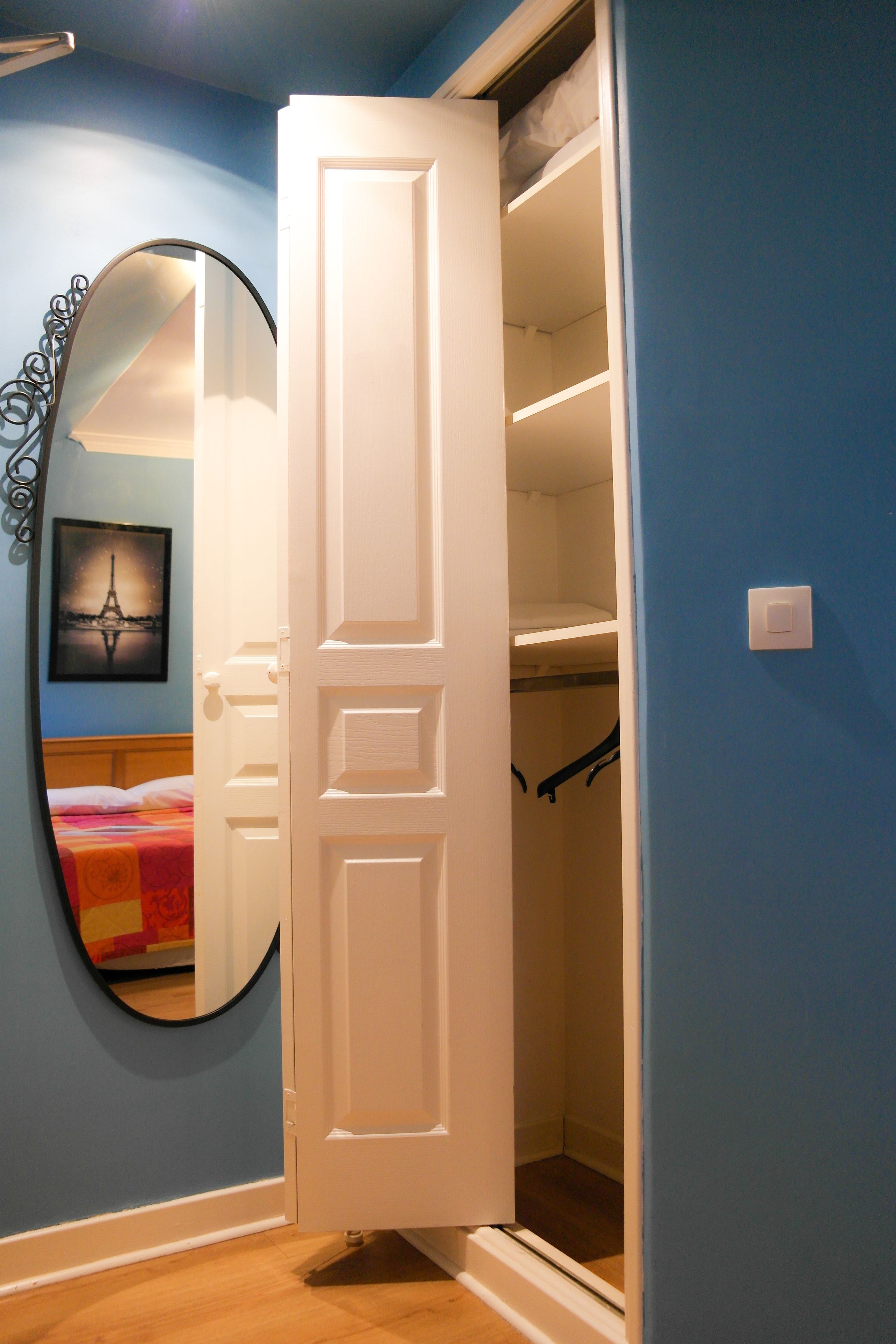 Una habitación con pared azul, puerta blanca y un espejo que refleja una cama con una manta colorida.