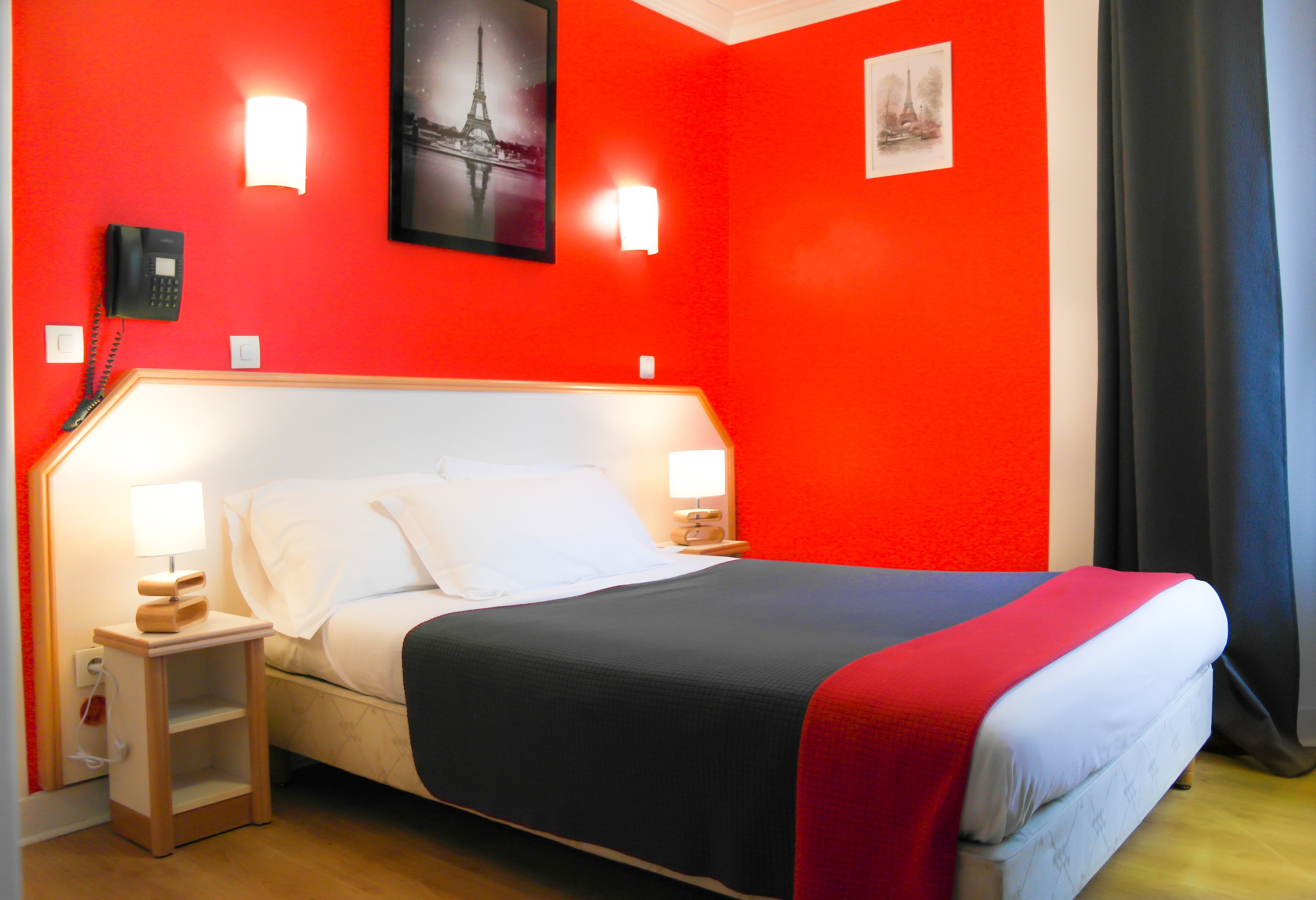A hotel room with a red wall, a bed with white bedding, two bedside lamps, a nightstand with a phone, and a small shelf.
