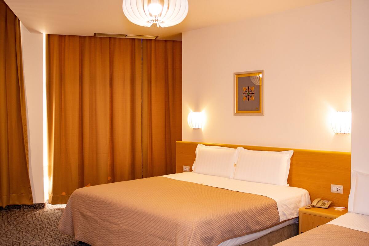 Ett hotellrum med en stor säng, ett nattduksbord med en telefon och en väggmonterad lampa.