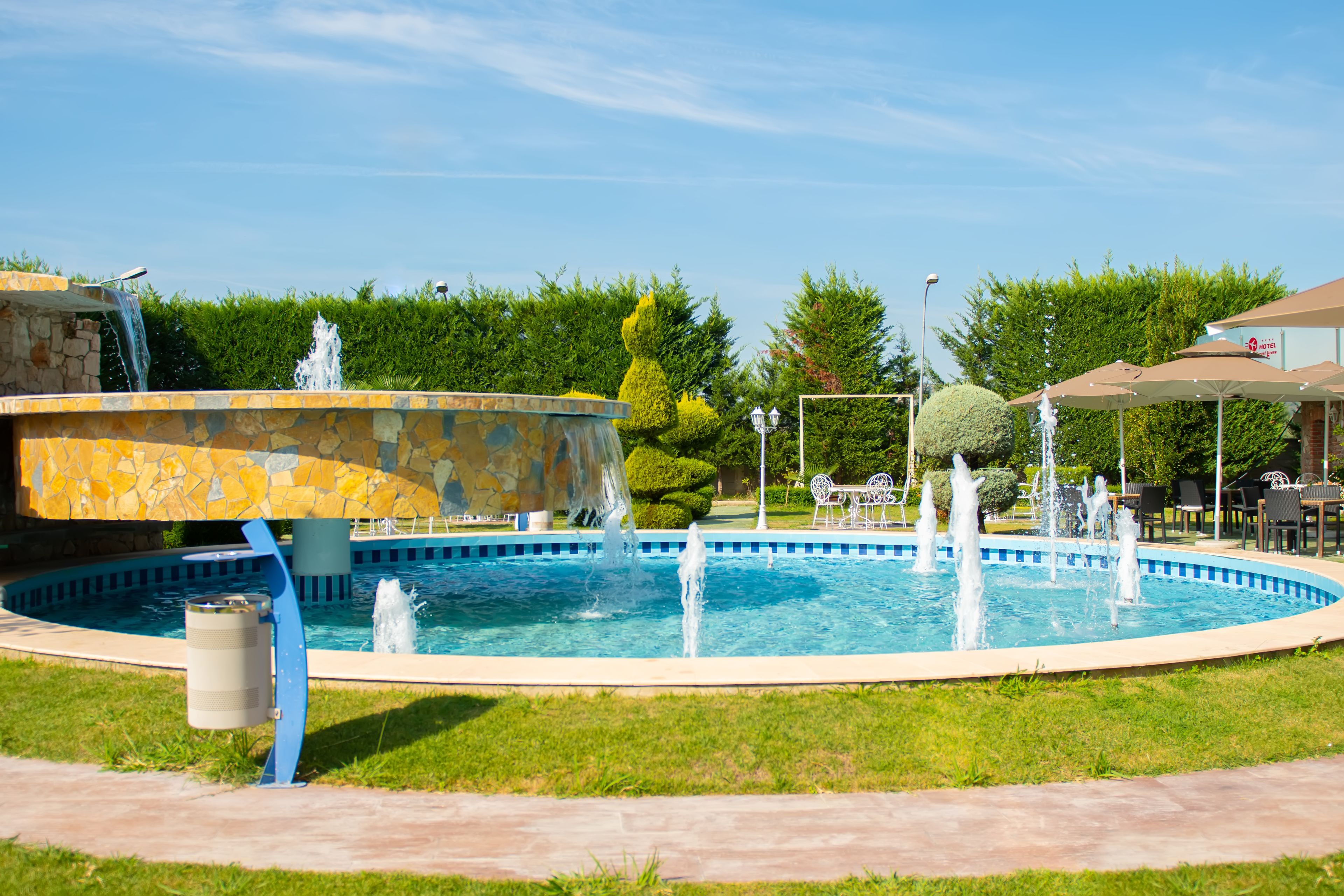 Una piscina con fuente, rodeada de césped cuidado y árboles.