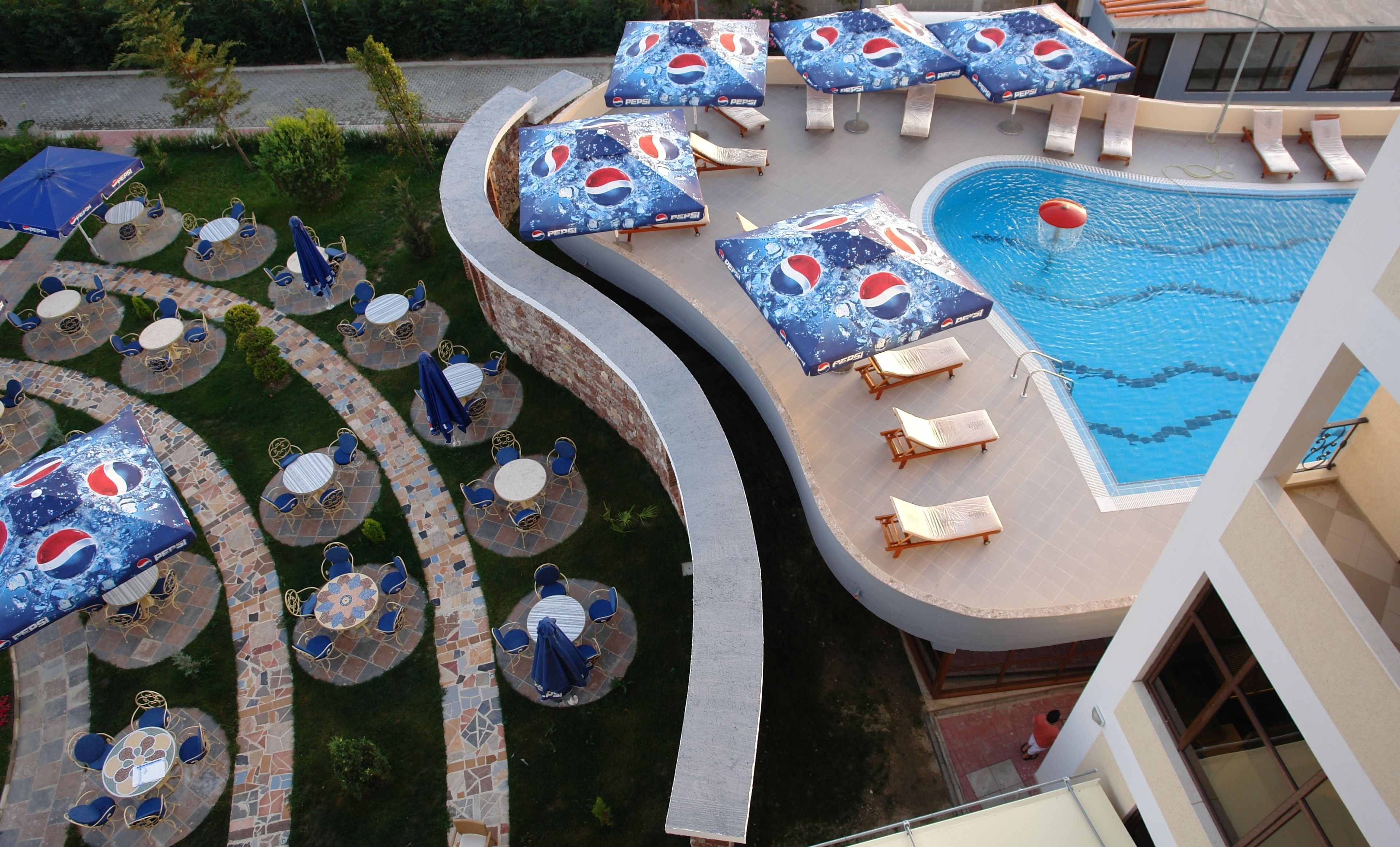 Un espace piscine doté de plusieurs chaises longues et de parasols, entouré d’une terrasse carrelée et d’un coin salon extérieur.