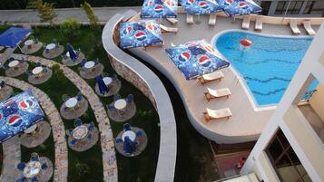 Un espace piscine doté de plusieurs chaises longues et de parasols, entouré d’une terrasse carrelée et d’un coin salon extérieur.
