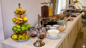 Une table de buffet proposant divers aliments, notamment des fruits, du café et du pain.