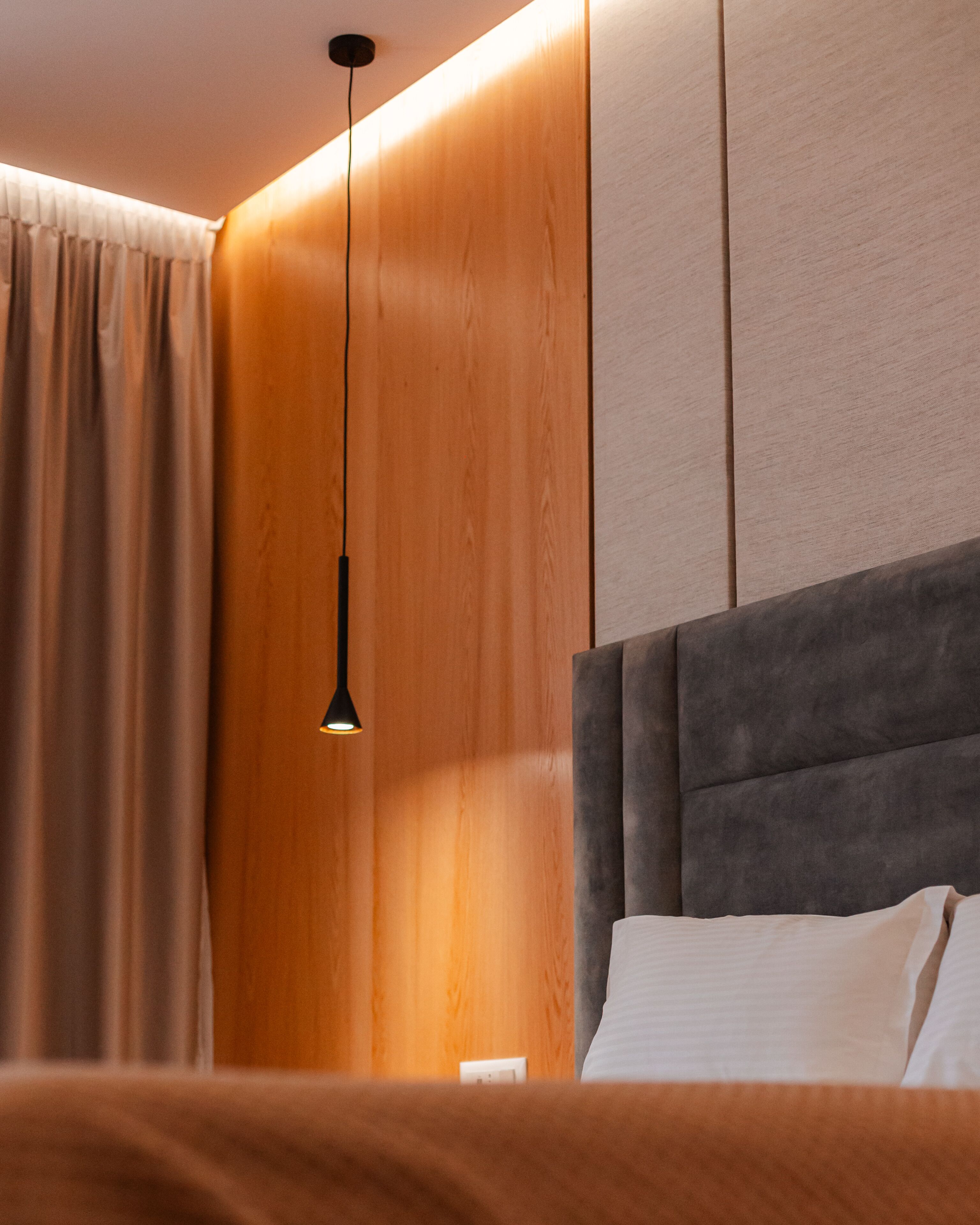 Una habitación de hotel moderna con una pared de acento de madera, un cabecero tapizado en gris y una lámpara colgante.