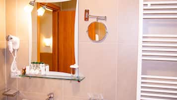 Un baño con repisas de vidrio que sostienen artículos de aseo, un espejo redondo, un perchero y un secador de pelo.