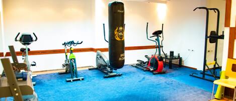 A gym with exercise equipment, a punching bag, and a blue carpeted floor.
