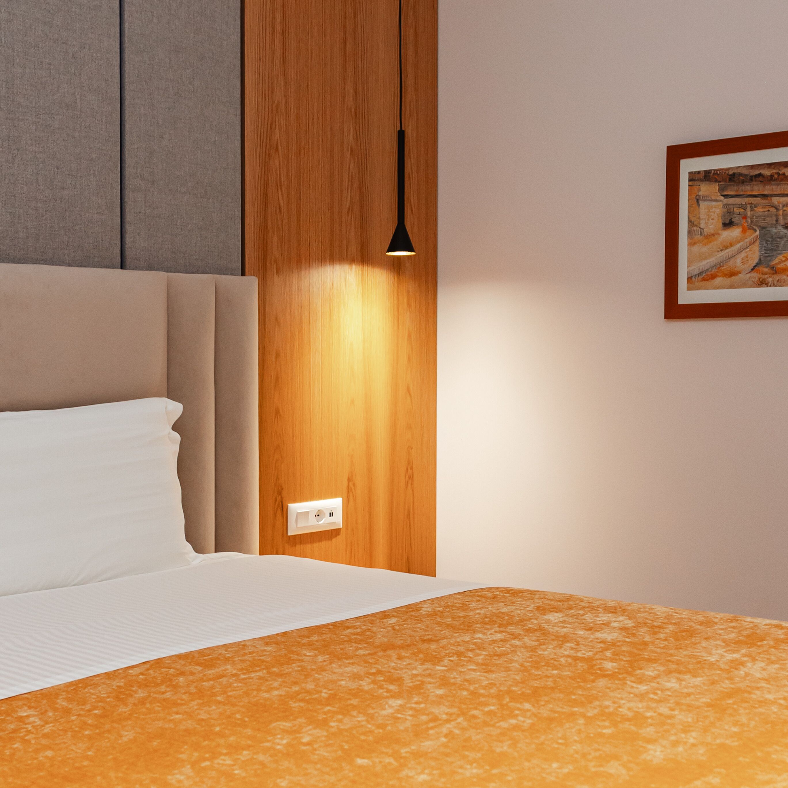 A hotel room with a bed, a wooden panel wall, a painting, and a light fixture.