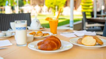A table with breakfast items including croissants, bread, a glass of orange juice, and a milk drink.