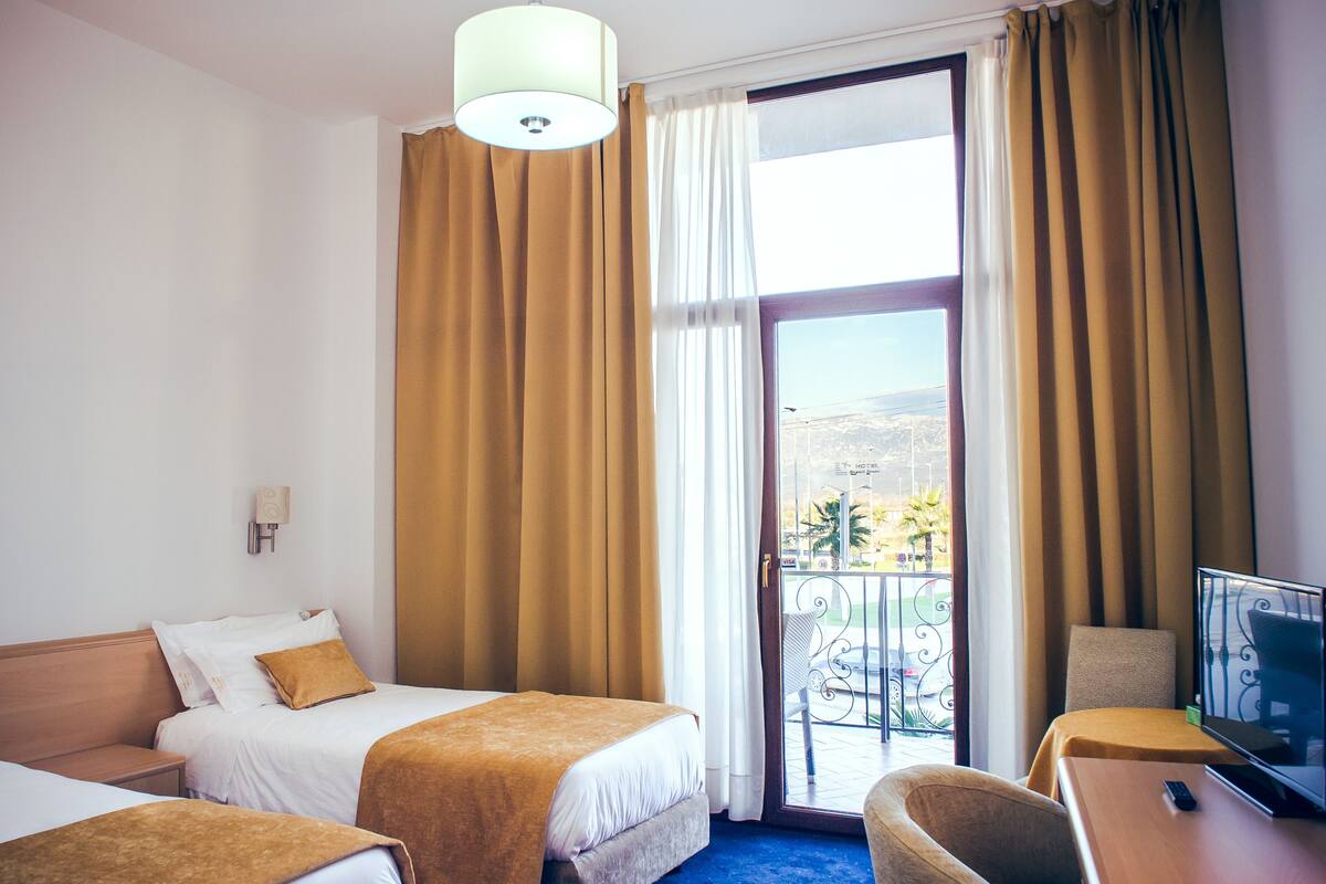 Ett hotellrum med två sängar, en tv och en balkong med utsikt över palmer.