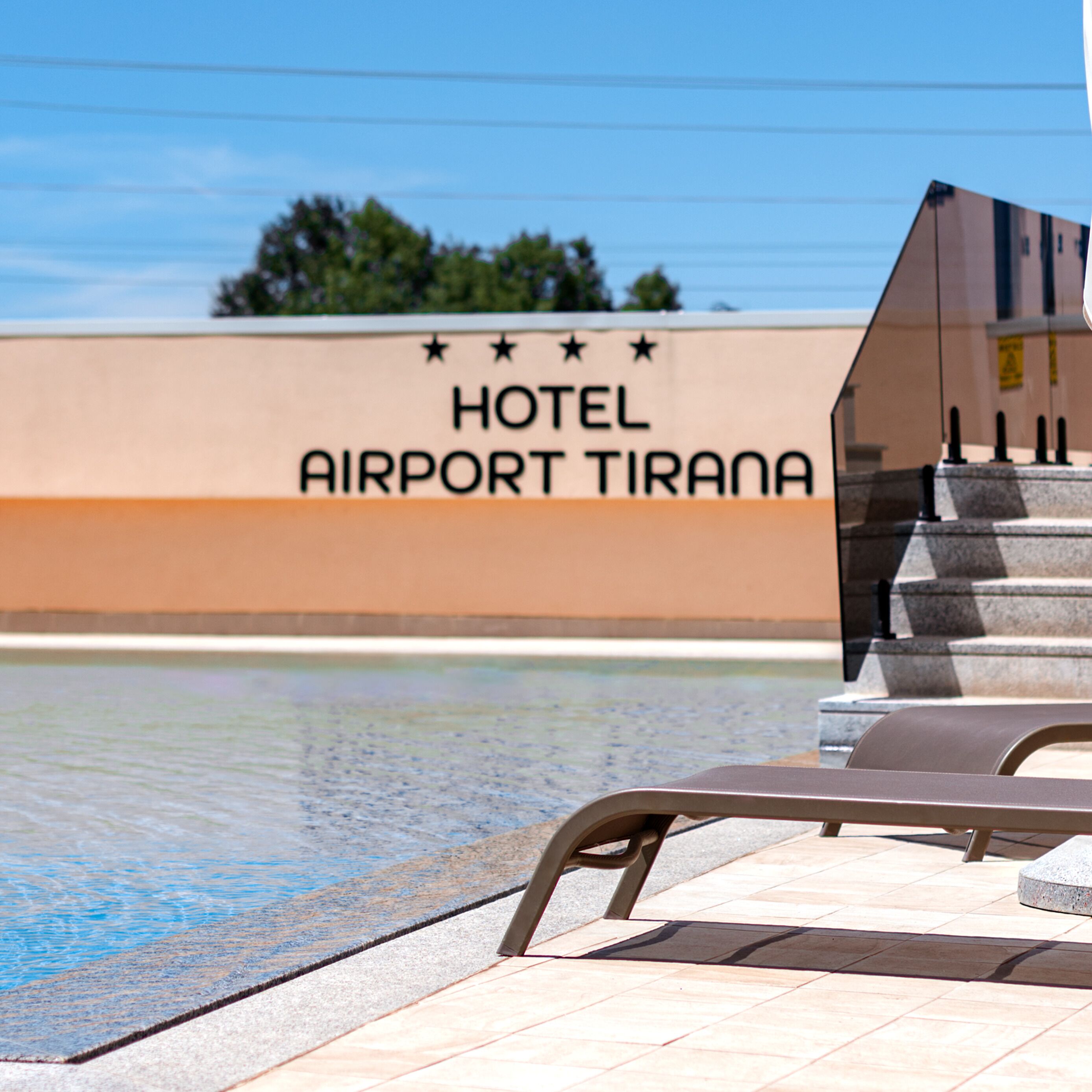 A pool area with a sign reading "HOTEL AIRPORT TIRANA" and a staircase leading up to the hotel entrance.