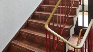 Una escalera con barandillas rojas y una planta en maceta en la plataforma.