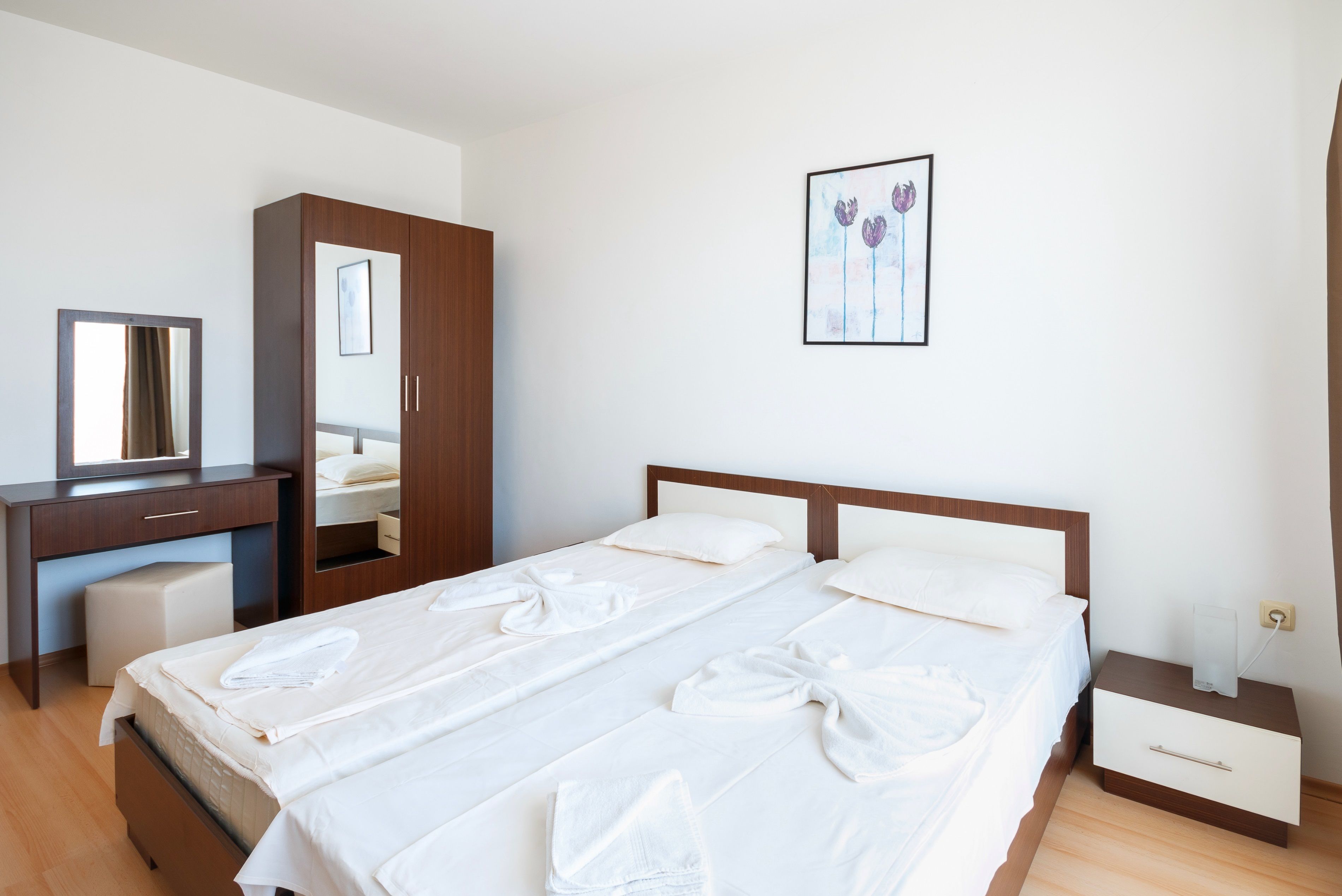 A hotel room with a bed, a desk, a chair, a wardrobe, and a bedside table.