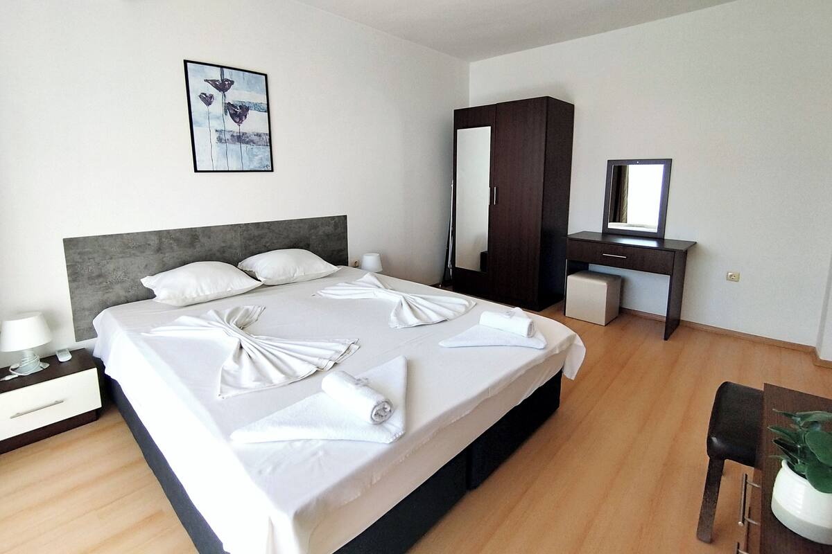 A hotel room with a neatly made bed, a desk with a mirror, and a framed picture on the wall.