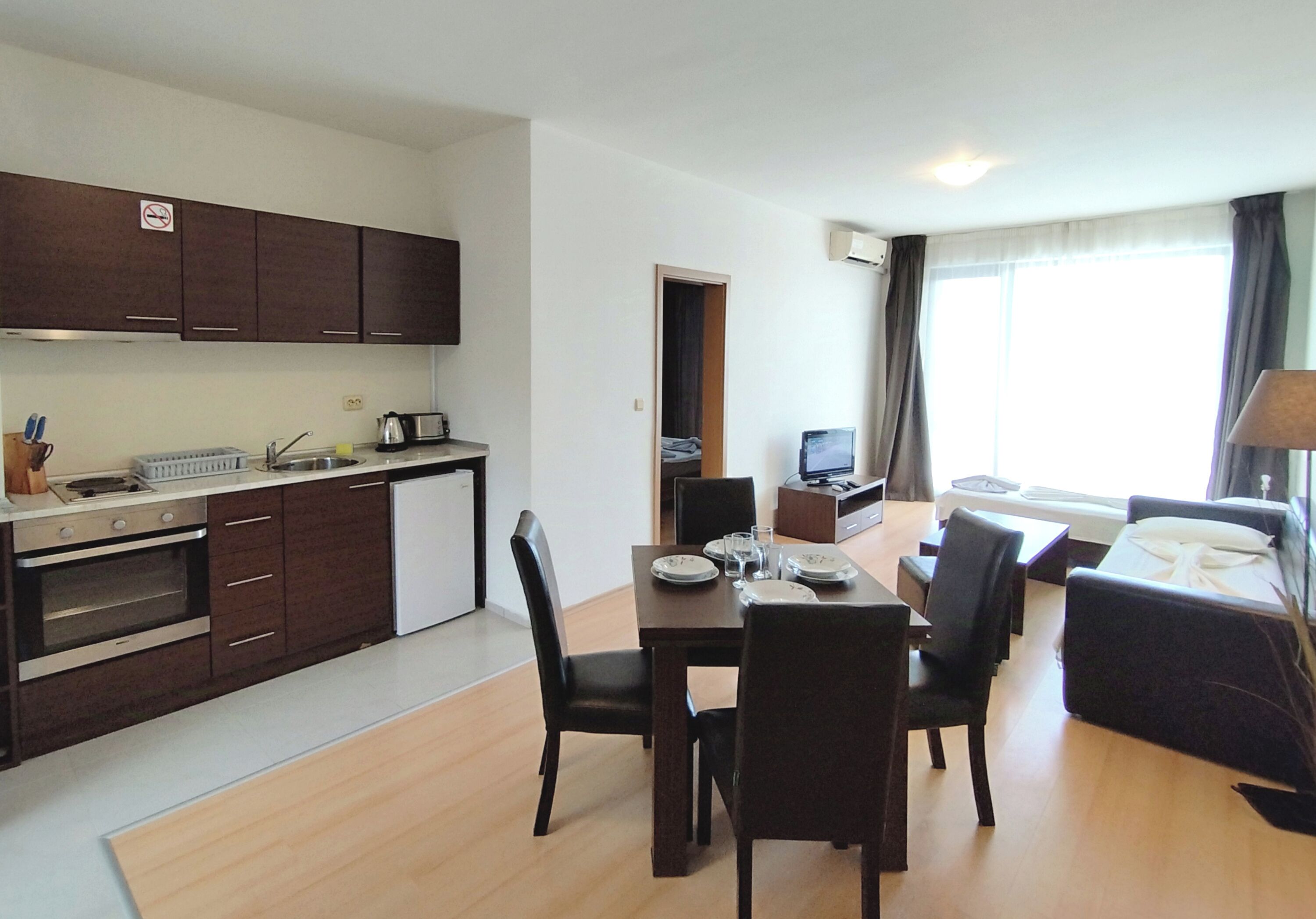 A compact hotel room with a kitchenette, dining area, and a bed.