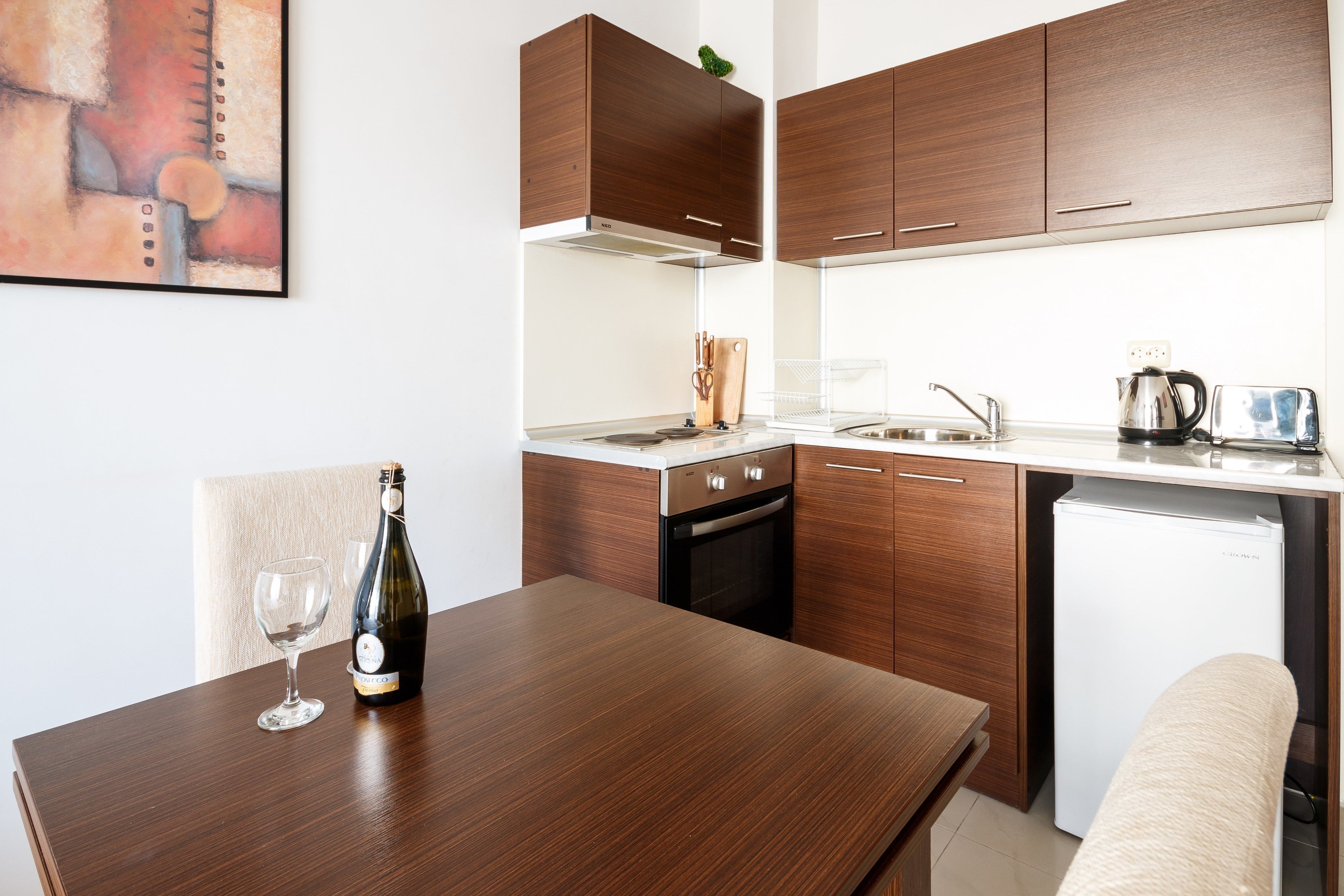 Et moderne køkken med træskabe, indbygget ovn, hvidt køleskab og spisebord med vinflaske og glas.