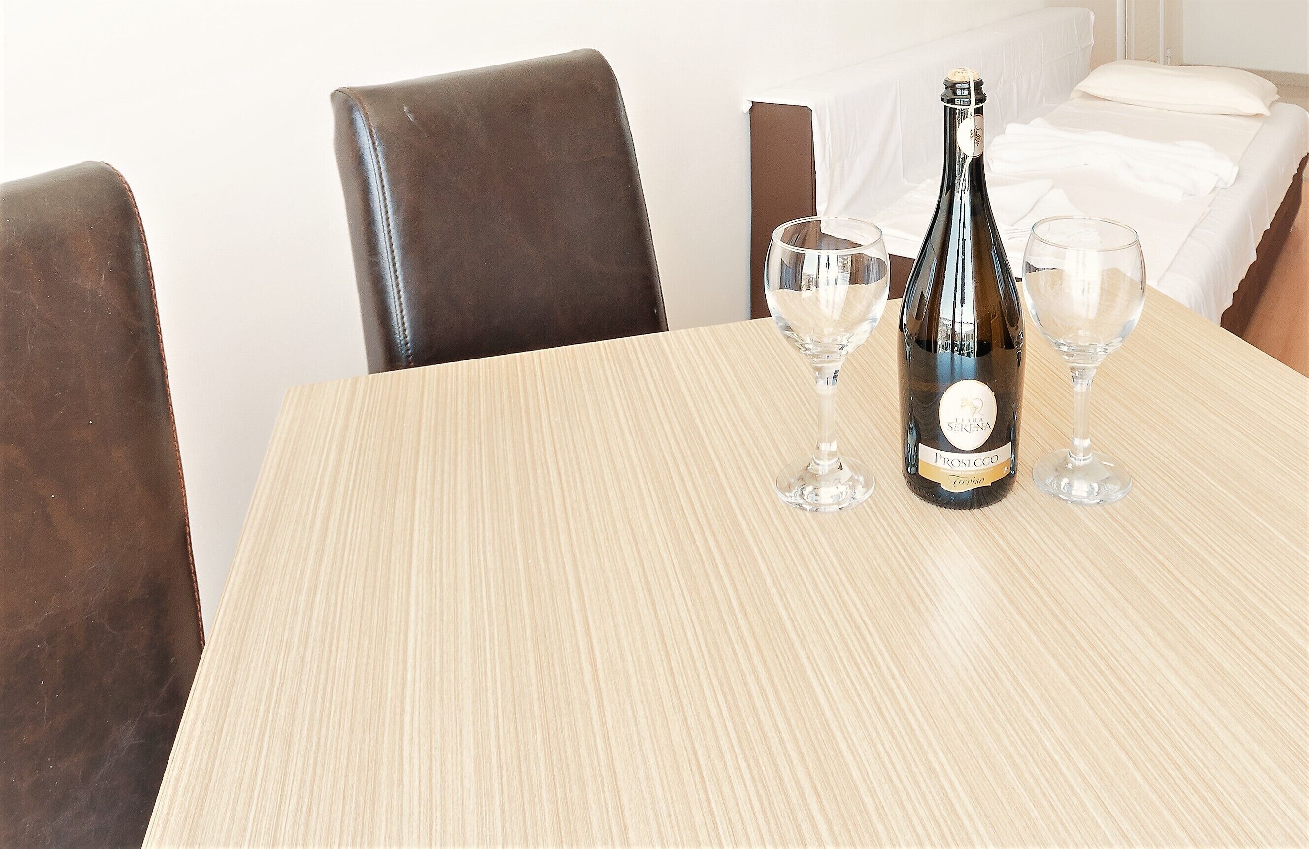 Una mesa con una botella de Prosecco y dos copas, rodeada de sillones de cuero marrón.