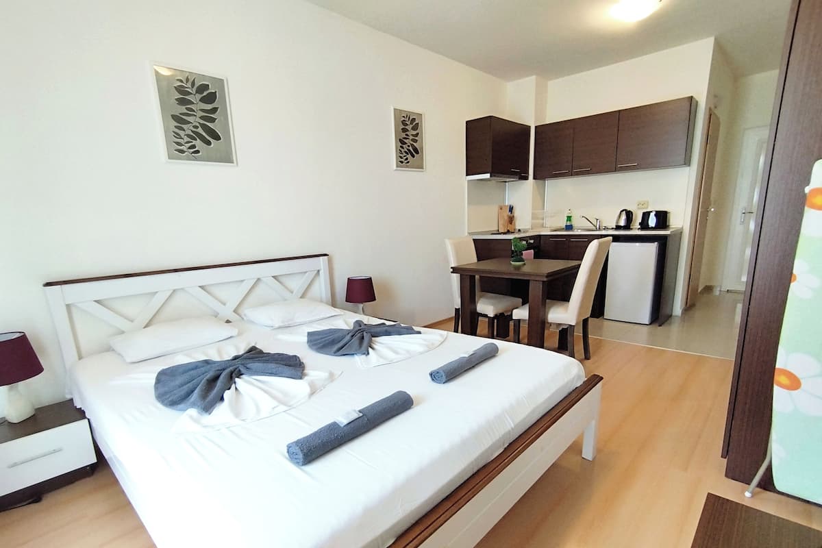A hotel room with a bed, bedside tables, a desk, and a kitchenette.