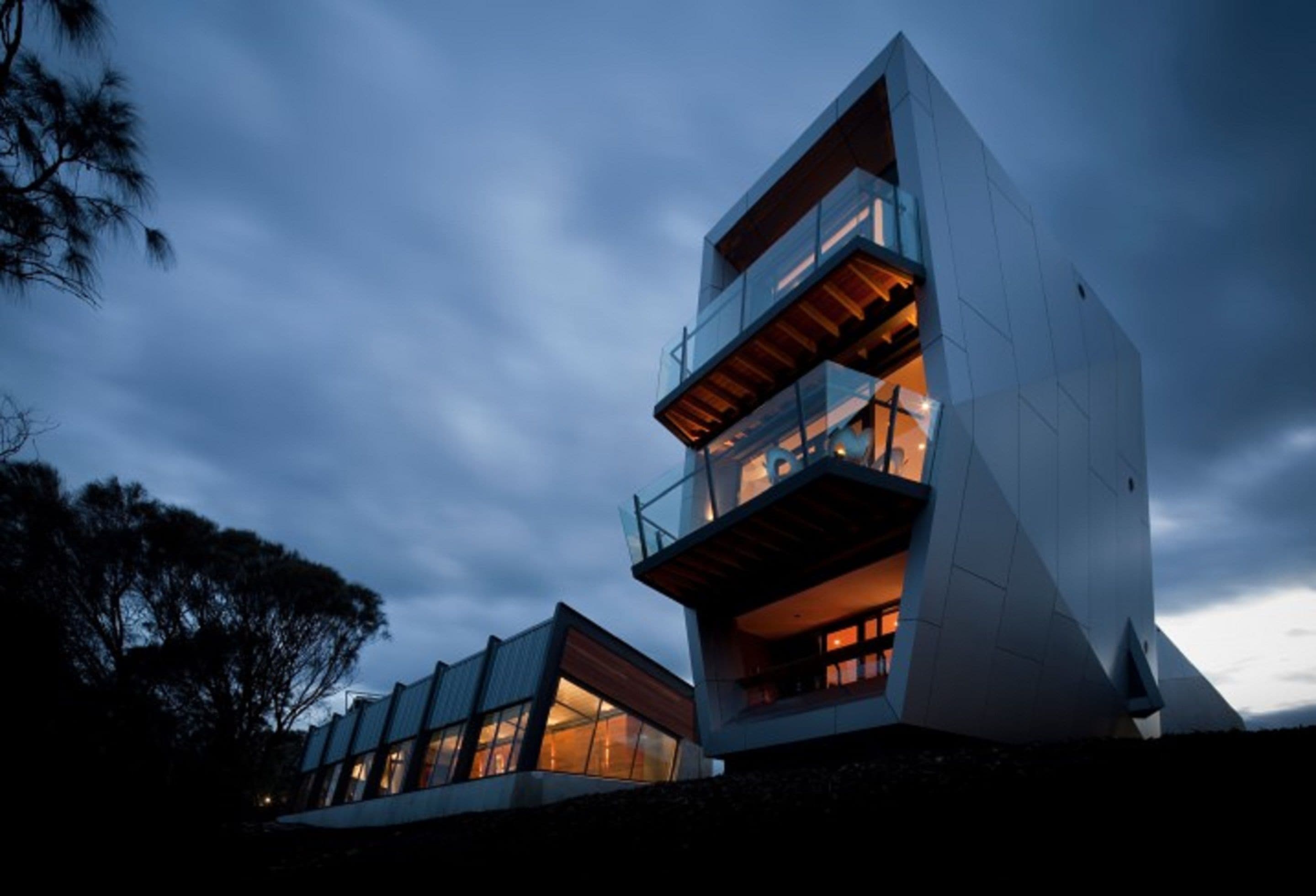 A modern multi-story building with large windows and balconies, set against a twilight sky.