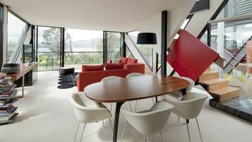 A modern interior with a wooden dining table, white chairs, red sofas, and a staircase.