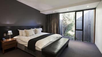 Une chambre moderne avec un grand lit, une table de chevet avec une lampe et une vue sur une terrasse en bois, accessible par une porte coulissante.