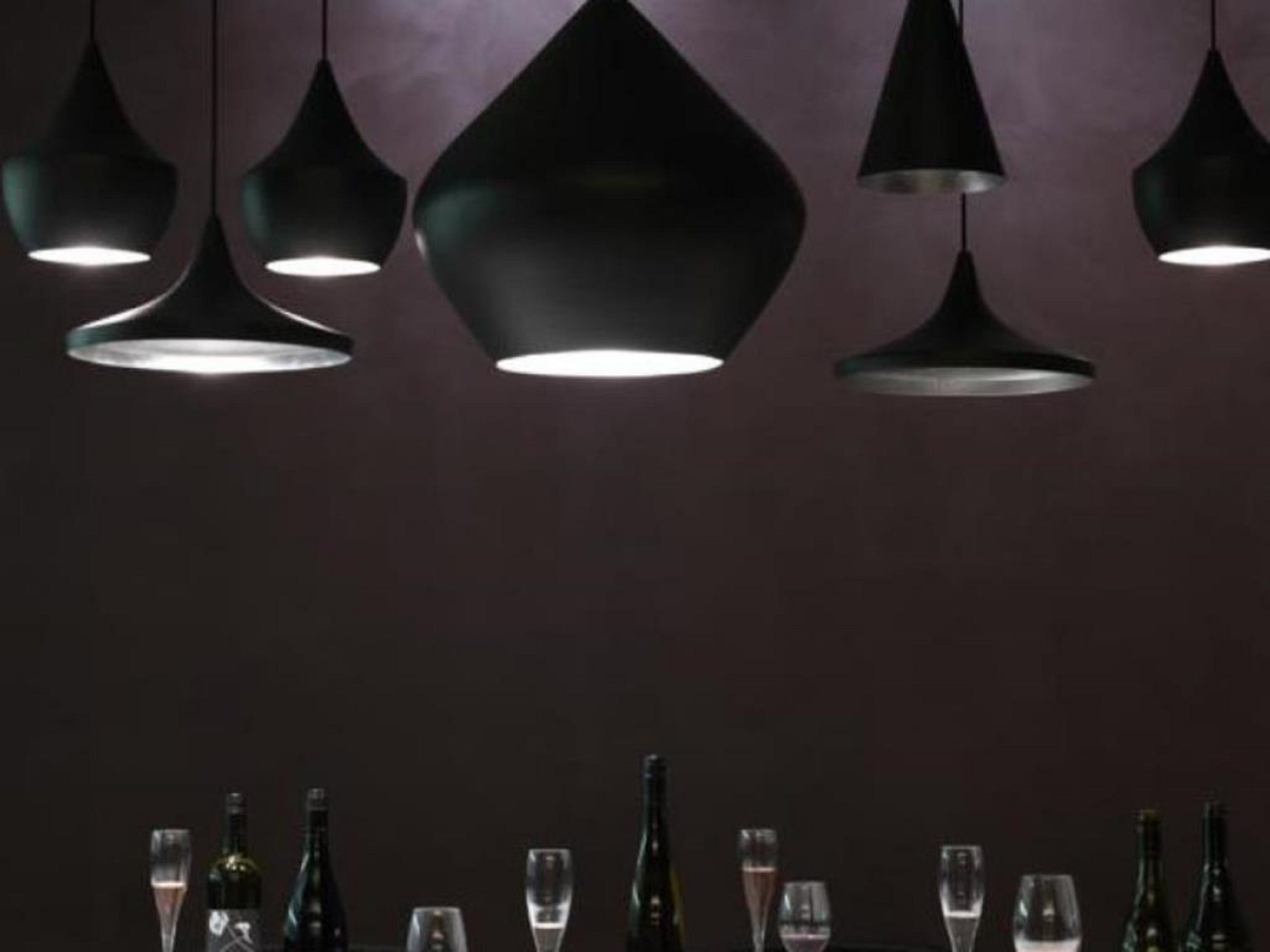 A dining area with multiple pendant lights and a table set with wine bottles and glasses.