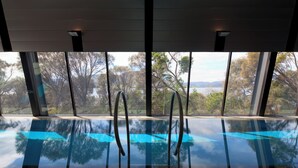 Una piscina interna con pareti di vetro trasparenti e ringhiere in metallo, che offre una vista su alberi e un paesaggio lontano.