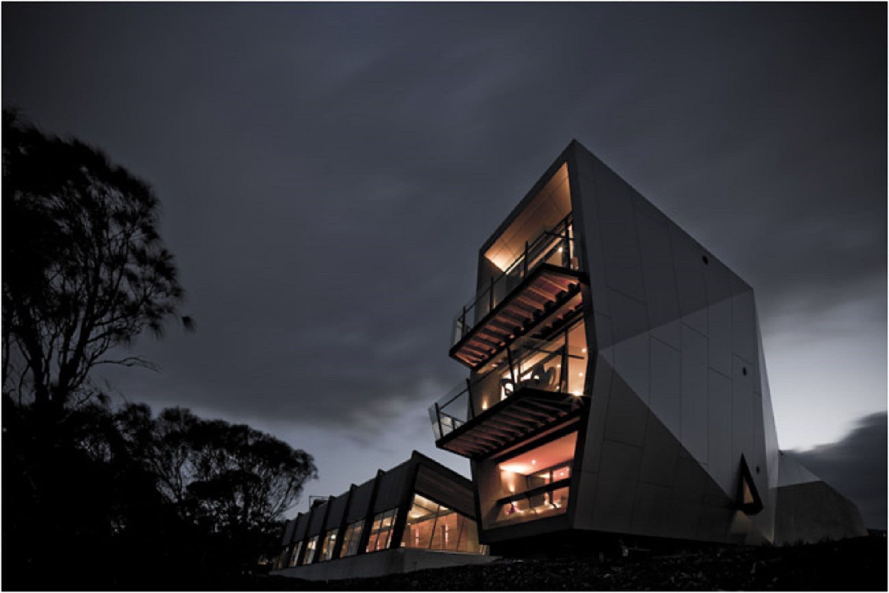 A modern multi-story building with balconies and large windows, set against a twilight sky.