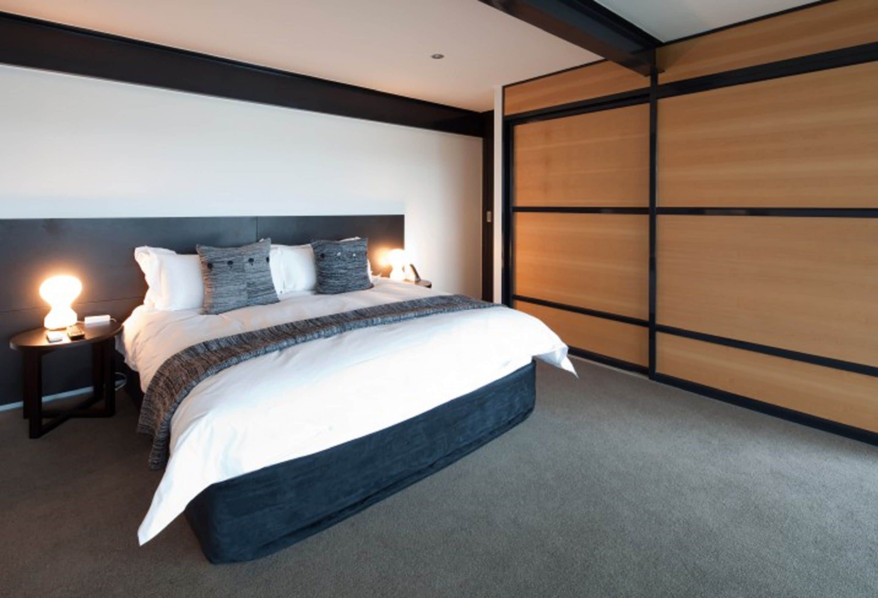 Un dormitorio moderno con una cama grande, cabecera oscura y una puerta corredera de madera.